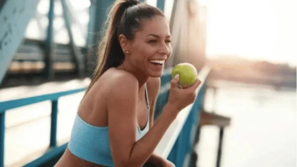 An active and healthy woman smiling while eating an apple.