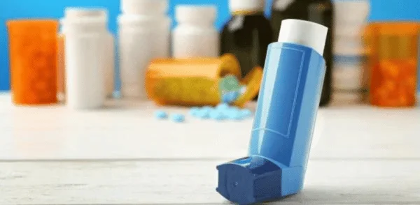 A blue asthma inhaler in the foreground, surrounded by other asthma medicines.