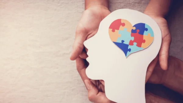 Hands holding human face shaped cardboard with heart made of puzzles