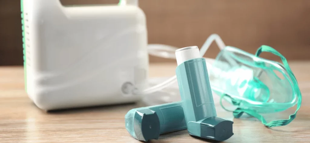 A photo of two blue asthma inhalers and a nebuliser in the background.